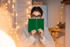 funny-young-woman-with-glasses-light-garlands-holding-book-her-hands-reading